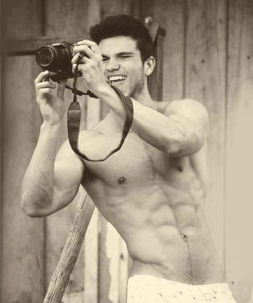 celeb taylor lautner with shirt off taking a photo with a camera and smiling