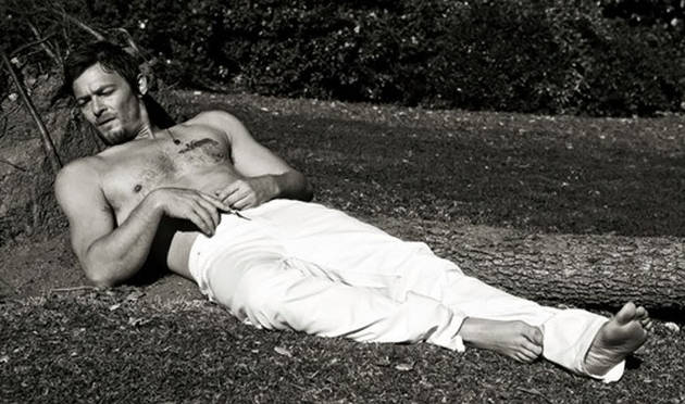 actor norman reedus with his shirt off laying on the ground black and white pic