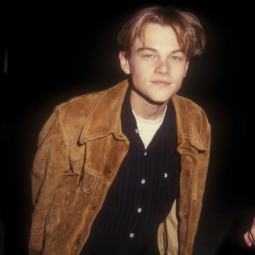 a young picture of famous actor leonardo dicaprio in a tan jacket smirking at the camera