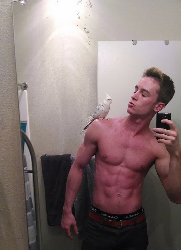 model and actor ryan kelley taking a shirtless selfie with a bird on his shoulder