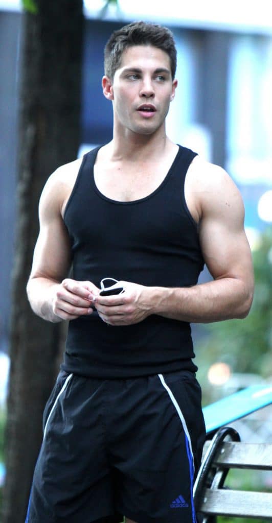 Dean Geyer with big muscles wearing black wife beater and shorts